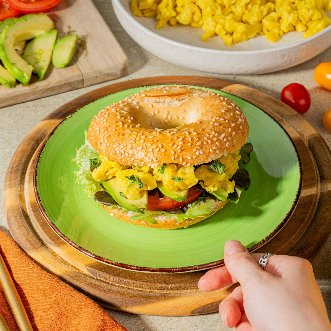 Breakfast Bagel mit veganem Ei, Avocado, Tomaten und Salat auf einem Teller mit weiteren Zutaten