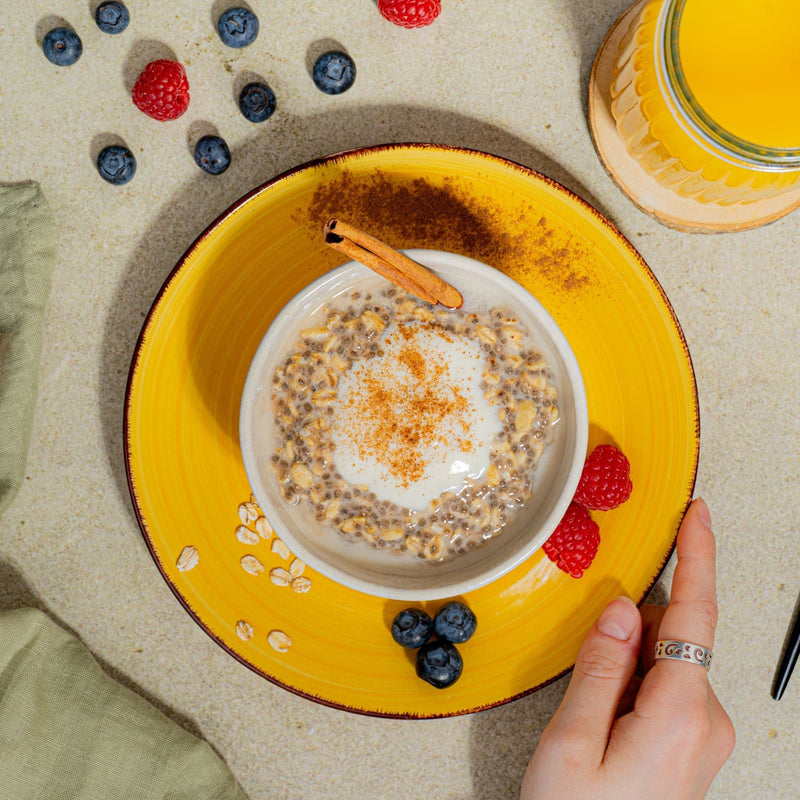 Vegane Overnight Oats getoppt mit veganem Joghurt und Zimt mit Beeren und Orangensaft.