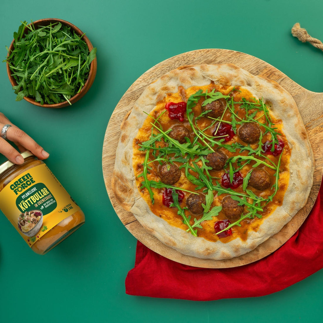 Vegane Köttbullar Pizza getoppt mit Greenforce Köttbullar Readymeal, Packung daneben, sowie ein Schälchen mit Rucola.