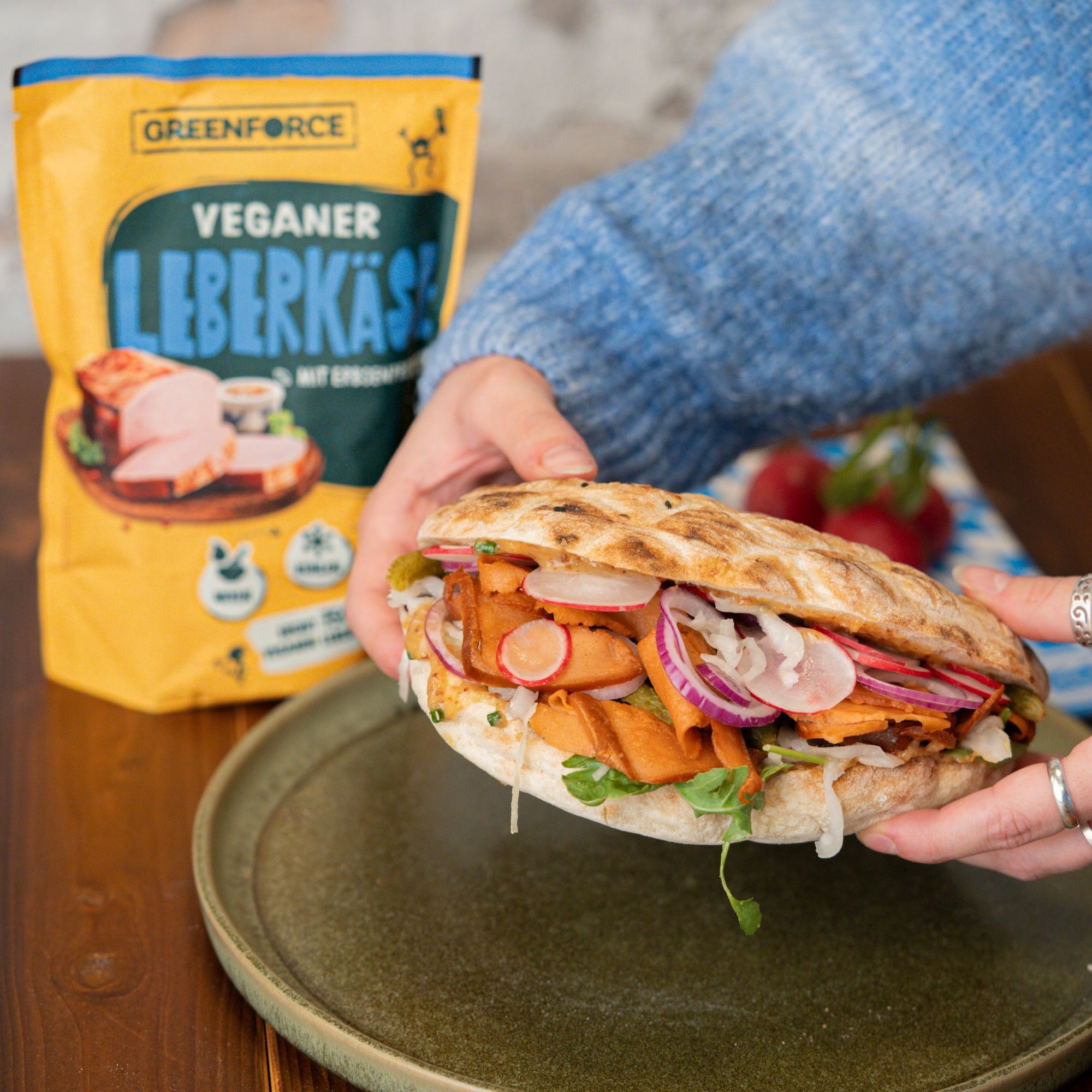 Person hält veganen Leberkäse Döner in den Händen mit GREENFORCE Leberkäse Packung im Hintergrund