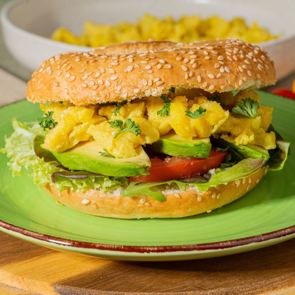 Close Up veganer Breakfast Bagel mit veganem Ei, Avocado, Tomate und Salat.