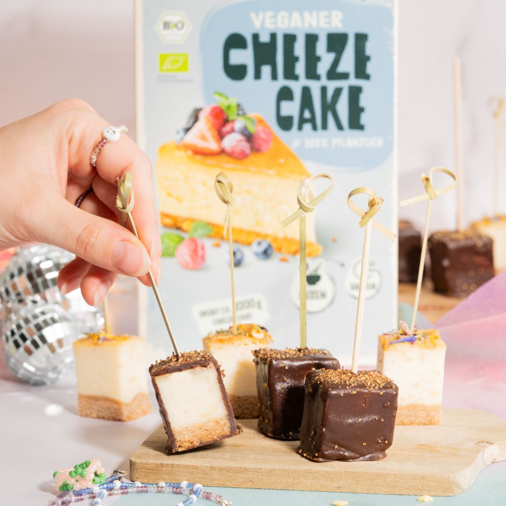 Mit und ohne Schokolade überzogene vegane Käsekuchen Häppchen mit der Greenforce Cheezecake Packung im Hintergrund