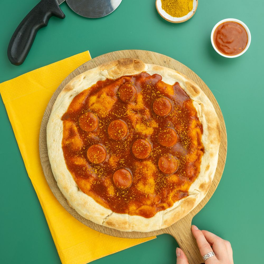 Vegane Currywurst Pizza mit Currysauce und Currypulver in kleinen Schälchen daneben