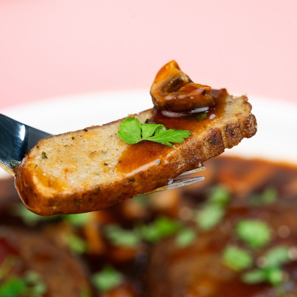 Close Up mundgerechtes Stück einer veganen Frikadelle mit Pilz-Bratensauce auf einer Gabel 