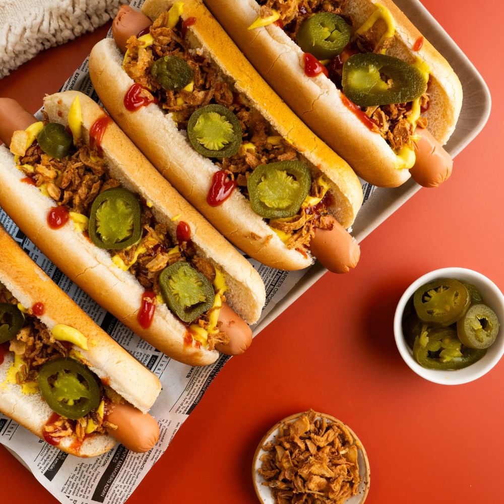 Platte mit Hot Dogs mit veganen Wienern, getoppt mit Ketchup, Senf, Röstzwiebeln und Jalapenos