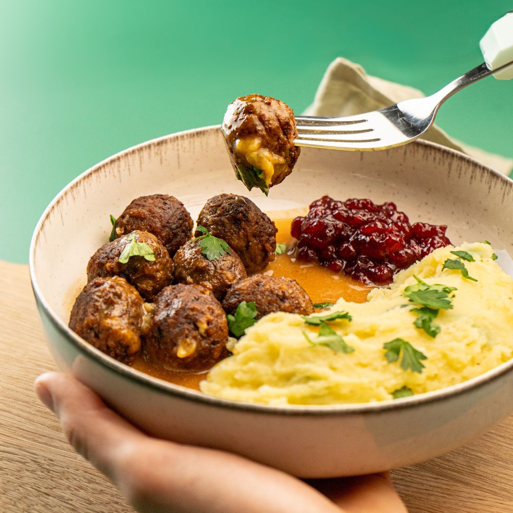 Veganes Köttbullarbällchen angspießt auf Gabel mit Rahmsoße und Kartoffelbrei im Teller