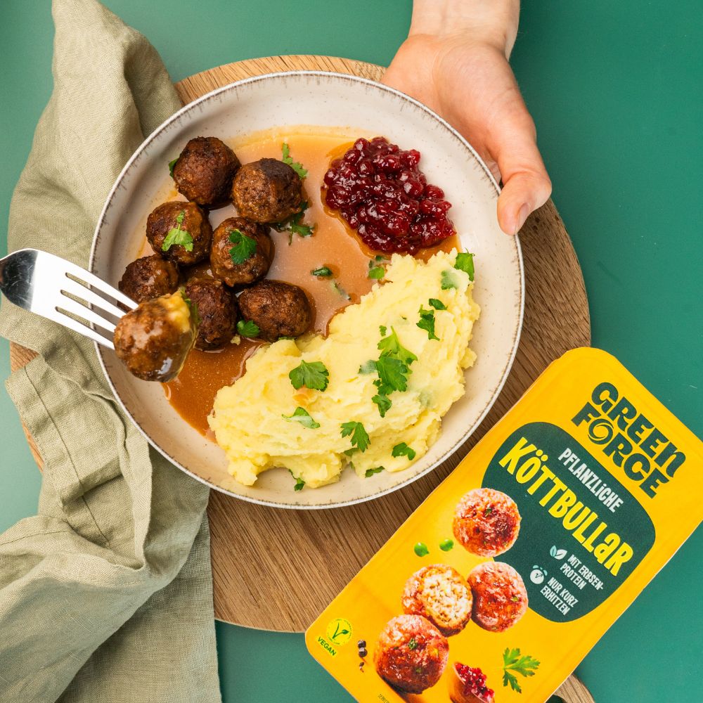 Vegane Köttbullar mit Rahmsoße und Kartoffelbrei im Teller von Person serviert mit Greenforce Köttbullar Packung daneben