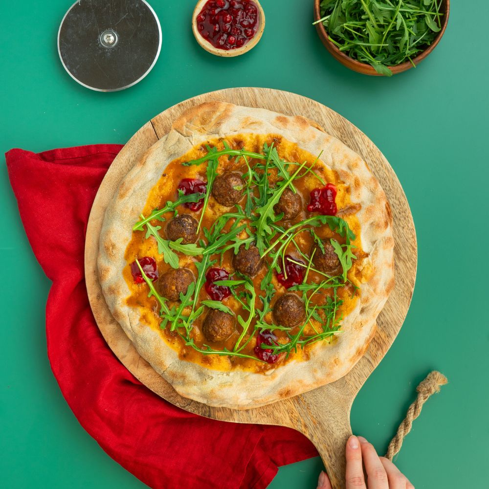 Pizza getoppt mit pflanzlichen Köttbullar, Cremesauce, Wildpreiselbeeren und Rucola.