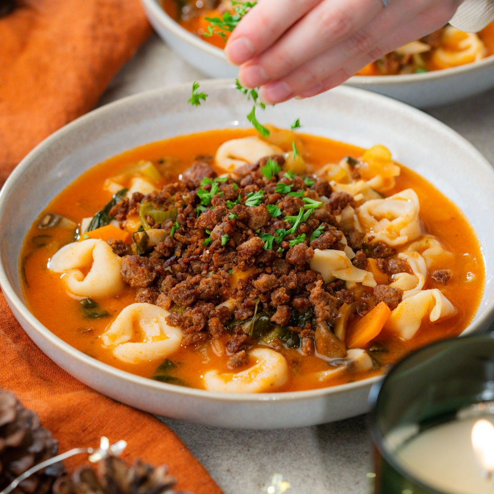 Hand streut Petersilie auf Tortellini Suppe mit veganem Hack